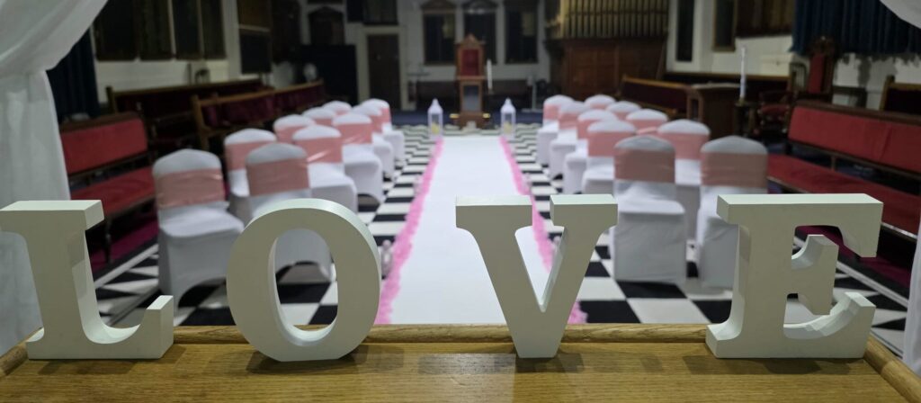 Wedding ceremony setup inside the historic Lodge Room at Beverley Road Masonic Hall in Hull, featuring white chair covers, pink sashes and decorative LOVE letters.